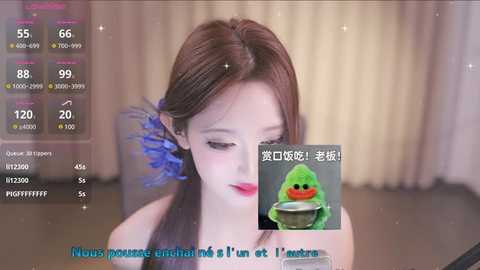 Media: A video of a young woman with long brown hair adorned with blue feathers, wearing a sleeveless top, sitting in a dimly lit room. She is holding a green toy.