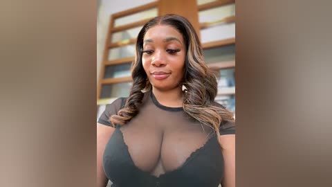 Media: Video of a Black woman with long, wavy, brown hair, wearing a sheer black top that reveals ample cleavage, standing indoors with wooden shelves in the background.