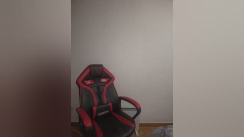 Media: A video of a modern gaming chair with red and black accents, positioned in a corner of a minimalist room with plain white walls and wooden floor, creating a clean, uncluttered space.