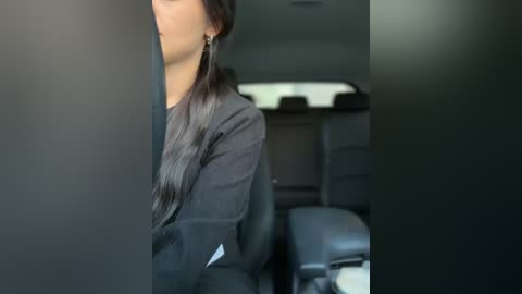 Media: Video of a woman with long black hair, wearing a black blazer, sitting in a dimly lit office with a blurred background of desks and chairs.