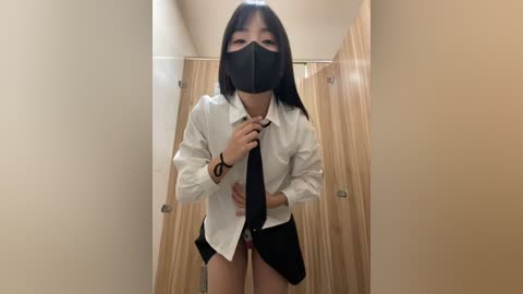 Media: A video of an Asian woman with straight black hair, wearing a white button-up shirt, black mask, and black tie, in a wooden-walled corridor.