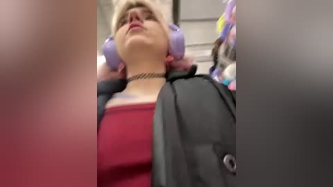 Media: A blurry video shows a woman with short blonde hair, wearing purple headphones and a black jacket over a red shirt, leaning back with a relaxed expression.