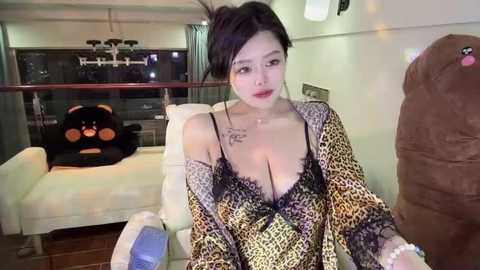 Media: Video of an Asian woman with dark hair, wearing a leopard print robe, sitting in a modern living room with a plush brown armchair and a white sofa.