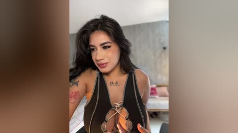 Media: Video of a Latina woman with long black hair, wearing a black halter top, tattoos on her arms, smiling, blurred background.