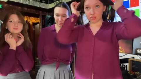 Media: Video of three young women in a bar, one fixing her hair, wearing purple shirts and grey skirts.