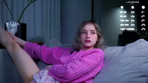 Media: Video of a young, blonde girl in a pink crocheted sweater, lying on a gray couch, looking at a TV displaying a sleep tracker.