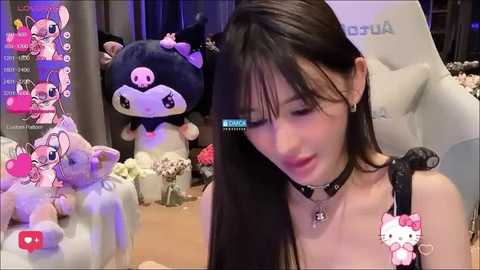 Media: Video of a young East Asian woman with long black hair, wearing a black choker, sitting in a plush chair with a large black cat plush toy beside her.