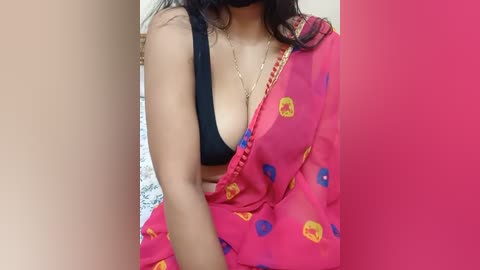 Media: Video of a South Asian woman with medium skin tone, wearing a black bra and a red sari with blue and yellow floral patterns, partially covering her breasts.