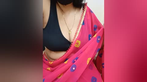 Media: Video of a woman with medium skin tone wearing a black bra and a pink sari with blue and yellow floral patterns, partially covering her chest.