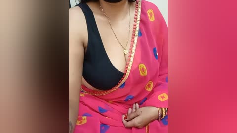 Media: Video of a woman in a bright pink sari with yellow polka dots, black bra visible, gold chain necklace, and red lipstick, against a pink background.