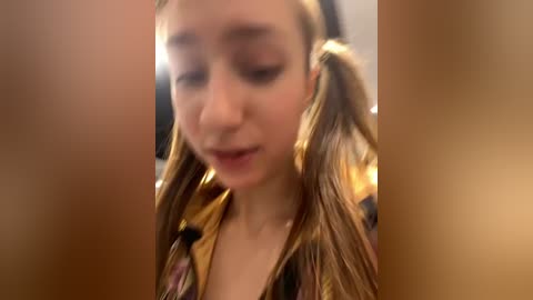 Media: A blurry video of a young girl with light skin and brown pigtails, wearing a floral blouse. Her eyes are closed, and she appears to be in a contemplative state. The background is out of focus.