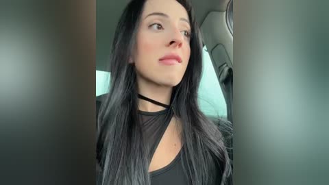 Media: Video of a fair-skinned woman with long, straight black hair, wearing a black choker and black top, looking upward with a neutral expression. Background features a car's interior.