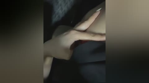 Media: Video of a close-up view of a person's hand, partially covered in black, touching their bare, light-skinned buttocks. The setting is dimly lit, creating a moody atmosphere.