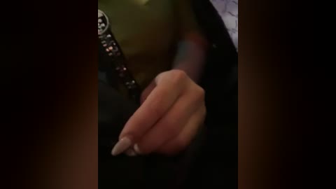 Media: Video of a person's hand, showing a clenched fist with neatly manicured nails, partially obscured by a dark, possibly black, sleeve. The background is dimly lit, creating a sense of mystery and intrigue.