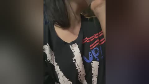 Media: Video of a woman with long brown hair wearing a black graphic T-shirt featuring white and blue text and designs.