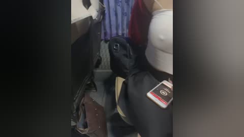 Media: A video captures a black dog wearing a white and yellow harness and leash, sitting in a cramped airplane bathroom. The dog's head is down, and a brown bag and red fabric are visible in the background.