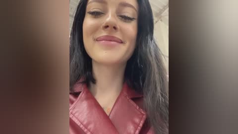 Media: A close-up video of a young woman with long, straight black hair, wearing a red leather jacket, smiling. Her eyes are closed, and her skin tone is light. The background is blurred.