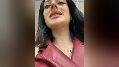 Media: Video of a smiling woman with long, straight black hair, wearing a red leather jacket and a necklace, with a blurred background.