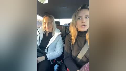 Media: Video of two young women seated in a car, wearing casual attire and driving with seat belts on. One has blonde hair, the other has darker hair.