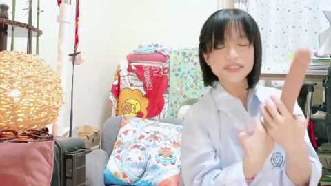 Media: Video of a smiling East Asian woman with straight black hair, wearing a blue robe, holding a smartphone, surrounded by colorful bags and a wicker basket in a cluttered room.