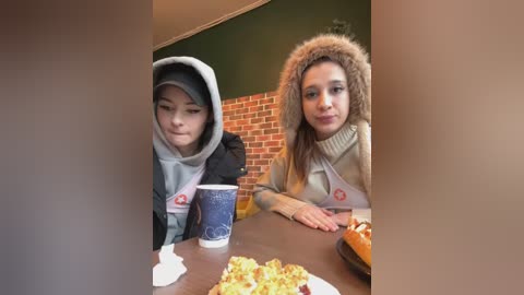 Media: Video of two young girls, one in a gray hoodie, the other in a fur-lined coat, eating at a table with a blue cup and plates of food.