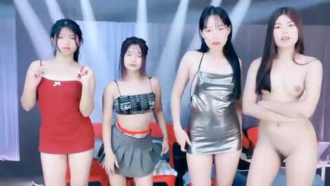 Media: Video of four Asian women, two fully clothed in red and silver dresses, and two nude, standing in a modern, brightly-lit room with white walls and red chairs.