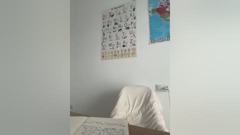 Media: A video of a child's room featuring a white wall adorned with a colorful alphabet poster and a world map, with a white chair and a book open on a desk.