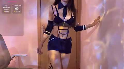 Media: Video of a slender, light-skinned woman with long dark hair, wearing a revealing black and white maid costume, standing in a dimly lit hallway with pink walls.