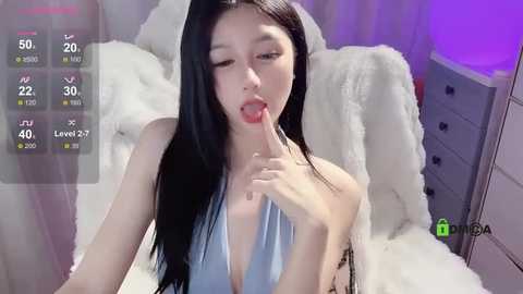 Media: A video of an Asian woman with long black hair, wearing a light blue halter top, seductively licking her finger in a bedroom with purple lighting.