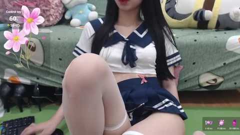 Media: Video of an East Asian woman with long black hair, wearing a revealing sailor schoolgirl outfit, sitting on a green bed with stuffed animals.