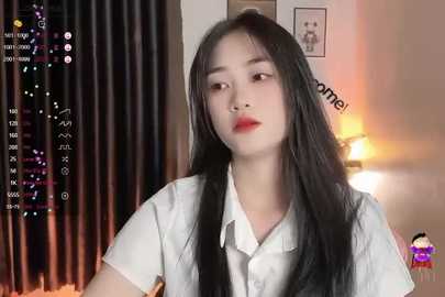 Media: Video of an East Asian woman with long black hair, wearing a white shirt, standing indoors with curtains and a lamp in the background.