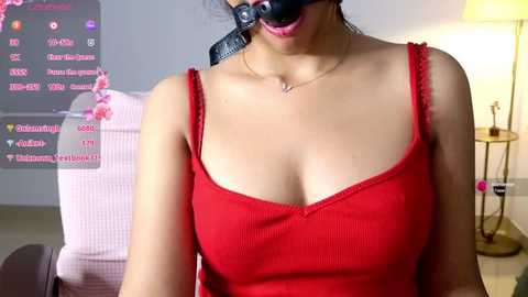 Media: Video of a woman in a red tank top, wearing a black leather mask with a strap, with a chat window displaying \"Twitch\" in the background.