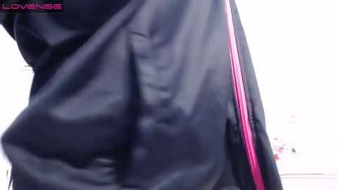 Media: Video of a person's lower back and buttocks, wearing a shiny black jacket with a pink stripe, taken from a low angle.