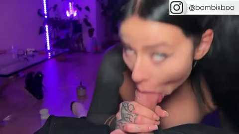 Media: A video shows a young woman with long black hair and pale skin, performing oral sex on a man. The room has purple lighting and scattered objects, including a bottle.