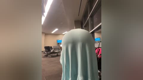 Media: A video of an empty airport terminal hallway with beige walls, fluorescent lighting, and a person wearing a light blue hijab in the background.