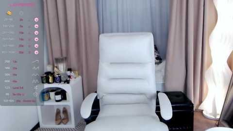 Media: Video of a modern, minimalist room with a white leather recliner chair, beige curtains, a white side table cluttered with items, and a pink digital calendar on the left.