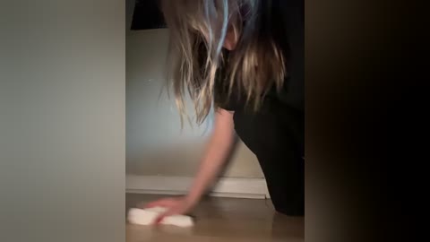 Media: A video captures a woman with long, wavy brown hair, bent over, cleaning a light-colored floor with a white cloth. She wears a black top. The scene is dimly lit, creating a moody ambiance.