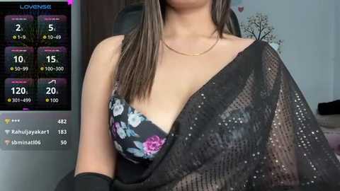 Media: Video of a woman in a black floral bra, wearing a sheer black scarf, indoors, with a digital screen displaying \"LOVENSE\" and stats on the left.