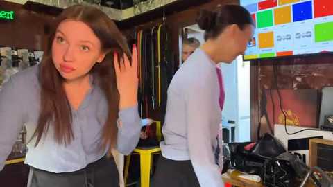 Media: A video shows two women in office attire adjusting their hair in a cluttered room with a colorful monitor and hanging jackets.