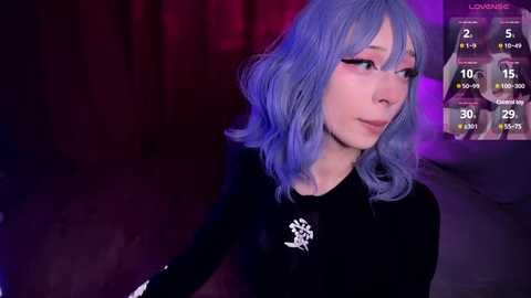 Video of a young woman with light blue, wavy hair and pale skin, wearing a black top with a Chinese character on it, in a dimly lit room with purple and pink lighting.