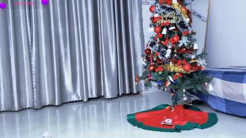 Media: Video of a festive Christmas tree with red, gold, and silver decorations, standing on a shiny white floor, next to silver curtains and a blue abstract wall painting.