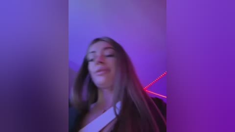 Media: A video of a young woman with long brown hair, wearing a white top, standing in a dimly lit room with purple and red LED lights, creating a moody, intimate atmosphere.