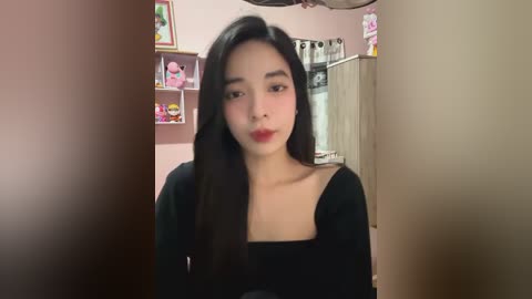 Media: Video of a young Asian woman with long black hair and fair skin, wearing a black top, standing in a pink room with cartoon-themed shelves and toys.