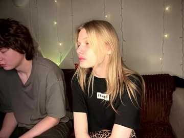 Media: Video of a young woman with long blonde hair in a black t-shirt and a leopard-print skirt, sitting on a brown couch, next to a man with dark hair in a grey t-shirt.