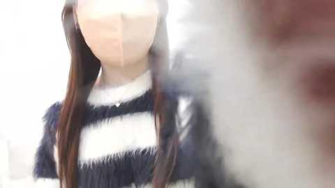 Media: Video of a person with long brown hair, wearing a white and black striped sweater, blurred background, and indistinct facial features.