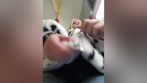 Media: A blurry video captures a person in a cow-patterned onesie, lying on a bed with hands near their face, blurred faces in the background.