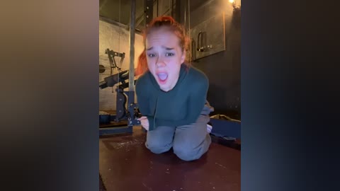 Media: A video of a terrified young woman with red hair, tied up and kneeling, in a dimly-lit, industrial room with a camera on a tripod.