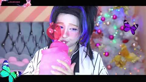 Media: A vibrant video of a young woman with fair skin and long black hair, wearing a white and black striped kimono, drinking from a pink milk bottle. Background features a festive, colorful room with butterflies and tinsel.