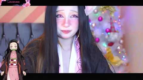 Media: Video of a young woman with long black hair, wearing a pink kimono and a mask, standing against a festive, colorful background with a decorated Christmas tree.