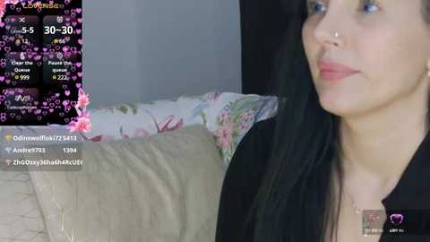 Media: A video of a woman with light skin and long black hair, wearing a nose ring, sitting on a floral-patterned couch. A live stream screen shows a chat with viewers.